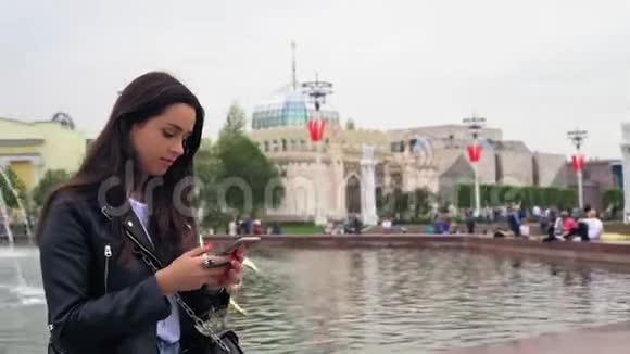 漂亮的年轻女人穿着黑色夹克使用现代智能手机4K视频的预览图