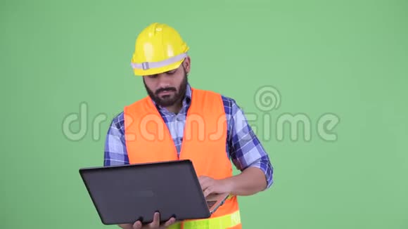 快乐年轻体重超重留着胡子的印度建筑工人正在思考如何使用笔记本电脑视频的预览图
