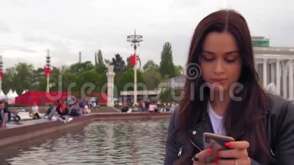 漂亮的年轻女人穿着黑色夹克用智能手机四处看看视频的预览图