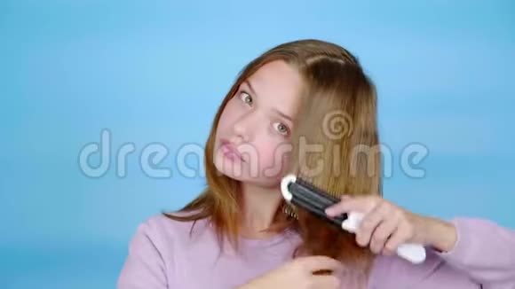 穿着粉红色套头衫的少女正用梳子梳头看着镜头视频的预览图