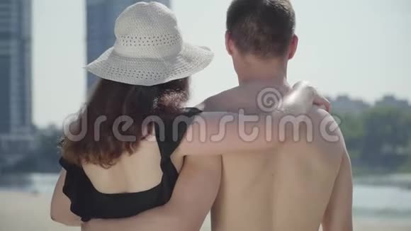 幸福的年轻夫妇拥抱着看着远处情侣们在炎热的夏日享受周末视频的预览图
