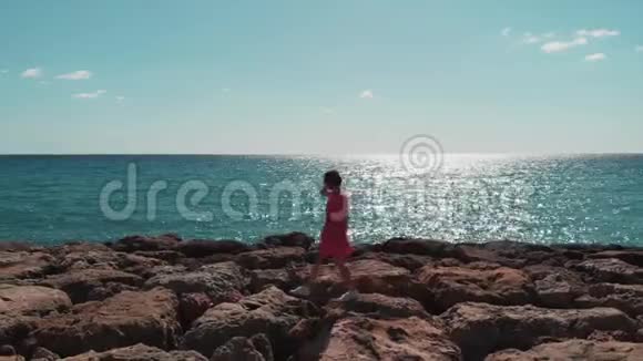 美丽的女人剪影独自走在岩石海码头海浪撞击岩石海滩太阳之路在碧海中的倒影视频的预览图