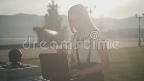商务女性穿着白色衬衫和眼镜坐在长凳上在笔记本电脑上工作这个女孩对这项工作很满意视频的预览图