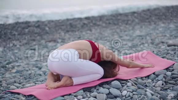 年轻女子穿着运动服在海滩上做瑜伽视频的预览图