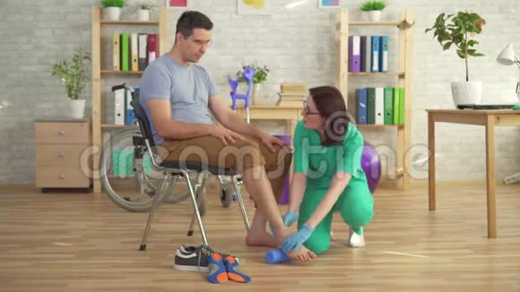 物理治疗师帮助轮椅上有骨科问题的人做运动用橡胶矫正平脚视频的预览图