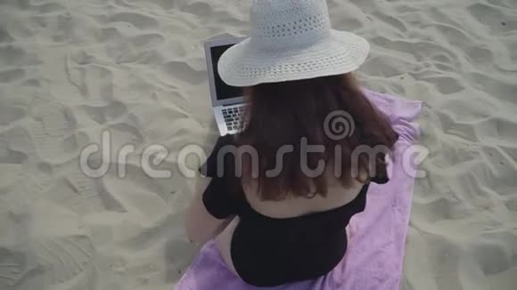 在海滩上年轻女子戴着白色帽子带着笔记本电脑工作自由职业概念忙碌的女人视频的预览图