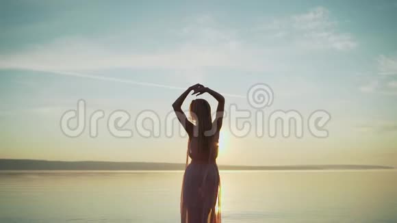 年轻女子穿着鲜嫩的红色连衣裙站在水面上在夕阳下享受着遥远的生活和自然视频的预览图