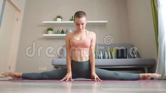 年轻女子在家训练瑜伽坐在垫子上伸展腿部肌肉视频的预览图