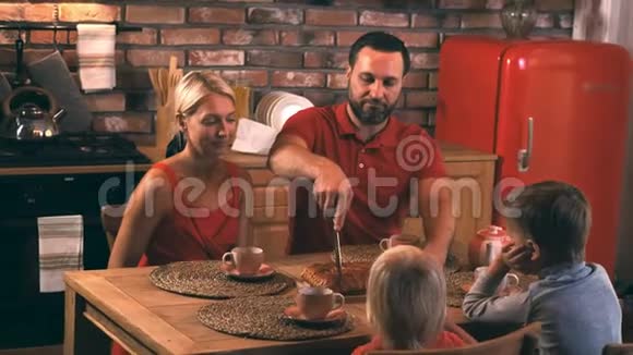 一个幸福的家庭在一个舒适的夜晚坐在厨房的桌子旁旁着妈妈烤的蛋糕吃晚饭视频的预览图