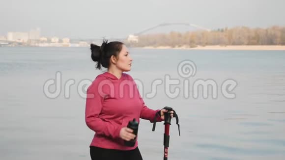 北欧式步行年轻胖乎乎的女人在市河附近的密集锻炼后从瓶子里喝水视频的预览图