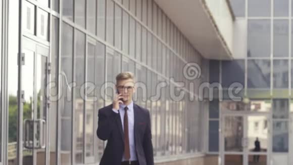 快乐迷人的白种人商人走在办公楼外用手机交谈他进来了视频的预览图