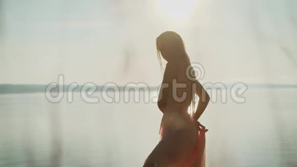 在日落的天空和太阳的背景下一个穿着连衣裙的女孩的剪影在草地下面她在跳舞这就是视频的预览图