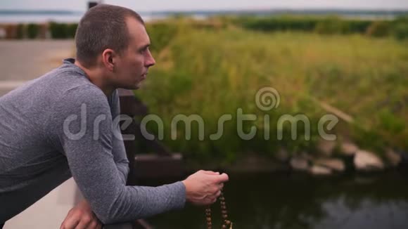 一个人站在一座桥上靠在一根木栏杆上手里拿着一个念珠一边看一边念祷告视频的预览图