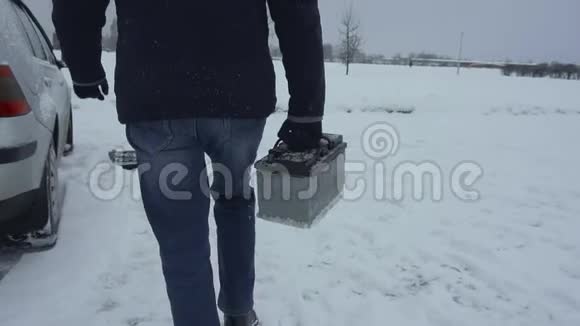 冬天人们手里拿着汽车电池开车在降雪时修理或修理坏的汽车故障视频的预览图