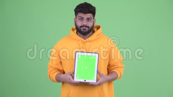 年轻体重超重留着胡须的印度男子展示数码平板电脑视频的预览图