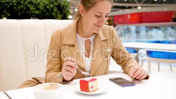 4k视频年轻女子坐在咖啡厅使用智能手机吃甜蛋糕视频的预览图
