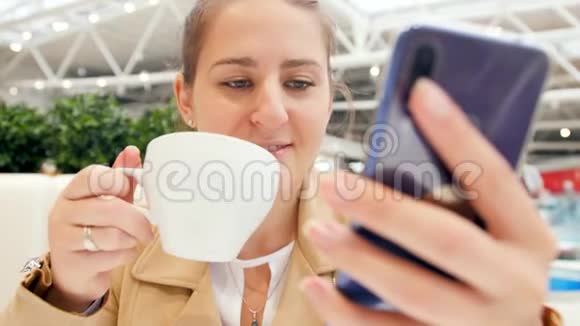 在自助餐厅喝卡布奇诺咖啡时年轻女子手持智能手机和打字信息的特写4k视频视频的预览图