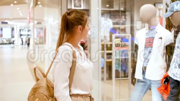 4k视频微笑的年轻女子在大型购物中心橱窗或橱窗后寻找新时尚服装视频的预览图
