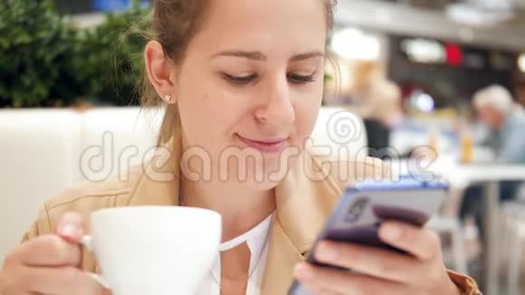 特写4k视频微笑的年轻女子在智能手机上浏览互联网在购物中心的咖啡馆喝咖啡视频的预览图