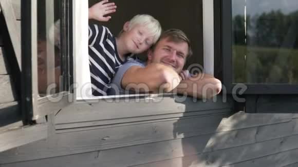 夏天一个男人带着一个金发男孩从农场木屋的窗户向客人道别视频的预览图