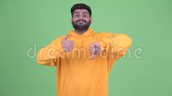 愚蠢的年轻超重留着胡须的印度男人在竖起大拇指和竖起大拇指之间做出选择视频的预览图