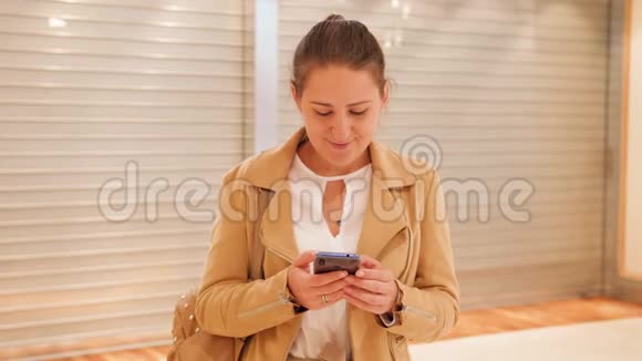4k视频年轻微笑的女人在智能手机上输入信息站在关门旁边看着镜头视频的预览图