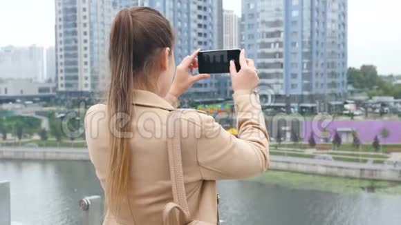 4k视频年轻女子站在屋顶在天际线和城市的智能手机上拍照视频的预览图