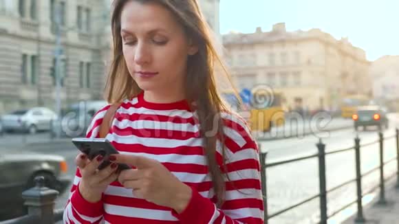 年轻女子站在老街日落时使用智能手机通信社交网络网上购物视频的预览图