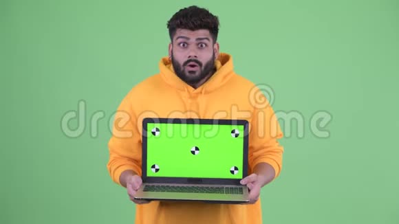 快乐的年轻体重超重留着胡须的印度男人带着笔记本电脑看上去很惊讶视频的预览图