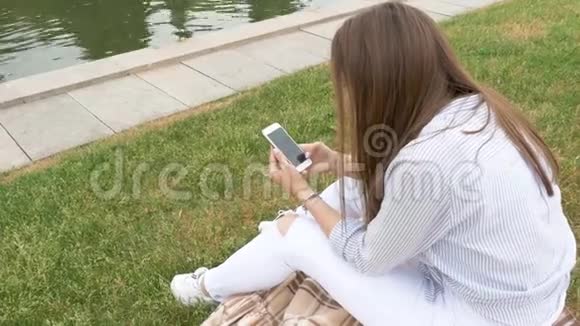 布鲁内特白色衬衫坐在草地上智能手机发送短信视频的预览图