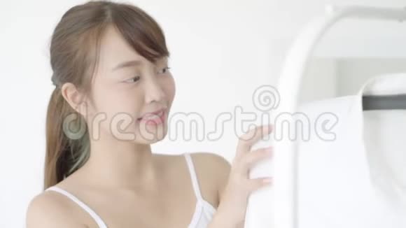 美丽的年轻亚洲女人从架子上挑选衣服房间里有衣架视频的预览图
