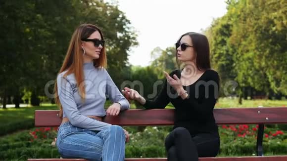 在阳光明媚的一天两个女朋友在公园里坐在长凳上聊天视频的预览图
