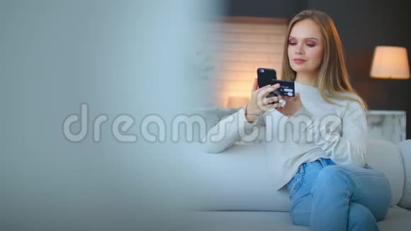 一个女人坐在沙发上用智能手机和银行卡在网上转账视频的预览图