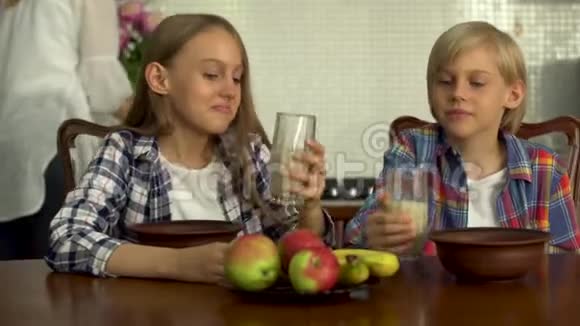 可爱的男孩和女孩喝透明眼镜的牛奶小兄弟在餐桌旁享用健康的饮料视频的预览图