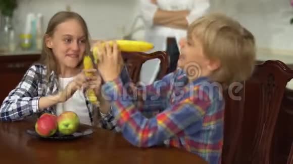 两个可爱的孩子在厨房里拿香蕉像武器一样胡闹男孩和女孩在一起健康视频的预览图