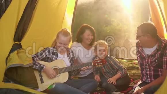 快乐的家庭在阳光下的露营帐篷里用吉他唱歌旅游家庭在露营中玩得很开心有趣搞笑视频的预览图