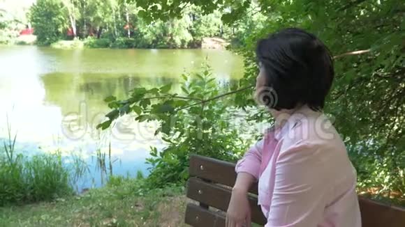 中年妇女在池塘附近休息坐在长凳上视频的预览图