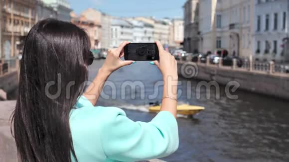 旅游妇女使用智能手机拍摄被历史名城包围的浮船河视频的预览图