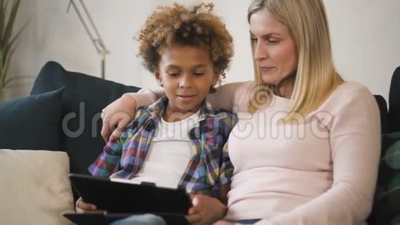 母亲和儿子坐在沙发上在笔记本电脑上看有趣的教育视频视频的预览图
