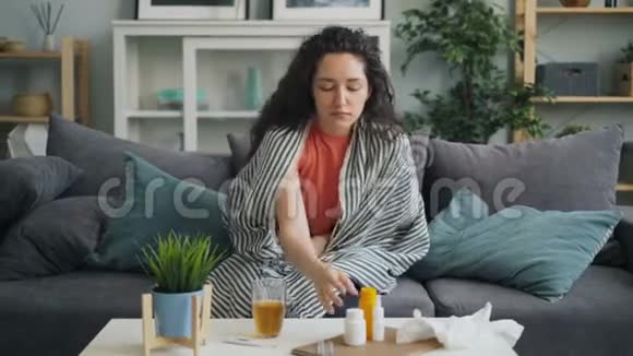 不舒服的女孩吃药喝着玻璃杯独自在家咳嗽视频的预览图