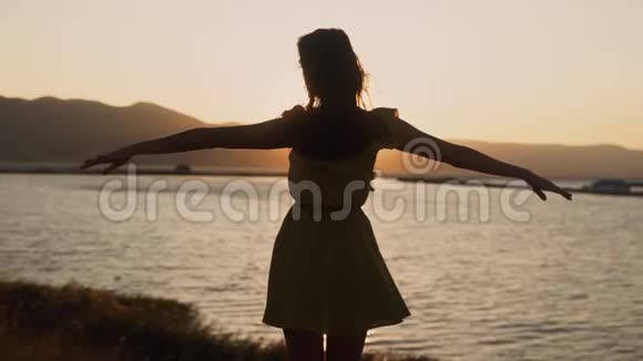 年轻女子的剪影在金色的夕阳下张开双臂动作缓慢视频的预览图