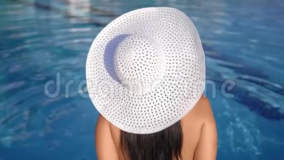 时尚晒黑的女性戴着白色帽子在游泳池旁享受日光浴后景特写视频的预览图