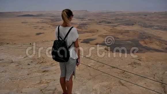 年轻女子背着背包站在悬崖边享受沙漠美景视频的预览图