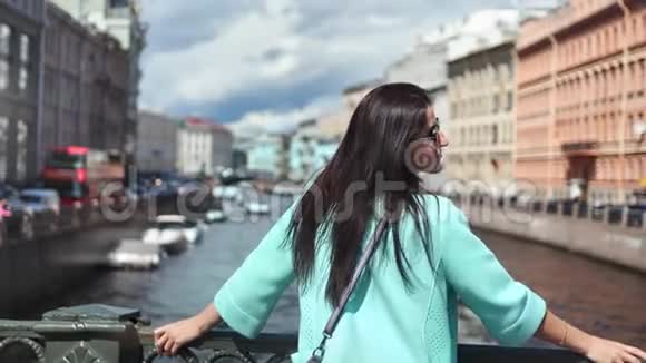 可爱的黑发旅行女人站在桥上欣赏令人惊叹的河流城市景观享受假期视频的预览图