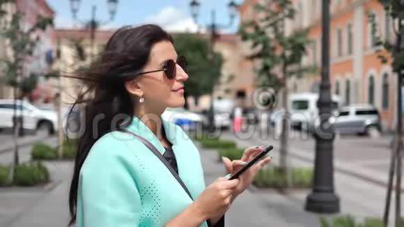 时尚迷人的女性在城市景观背景下使用智能手机挥动头发中等特写镜头视频的预览图