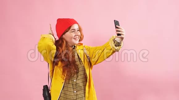 一个戴着黄色雨衣的红头发快乐女孩用智能手机拍摄的工作室画像视频的预览图