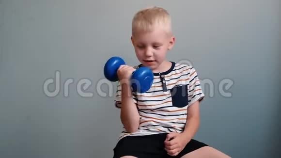 6岁的可爱男孩在灰色背景下用哑铃做运动视频的预览图