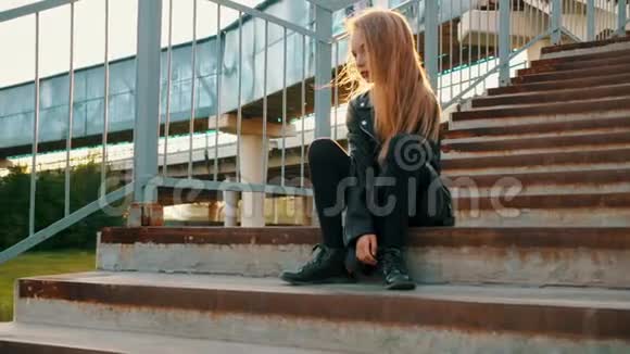 穿黑色皮夹克的年轻女孩坐在楼梯上时尚模特在楼梯上摆姿势穿皮衣服的摇滚女孩视频的预览图