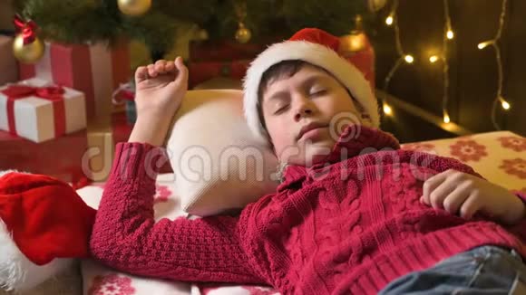 圣诞老人帮手男孩睡觉和等待圣诞老人躺在装饰的圣诞树附近灯光圣诞快乐和节日快乐视频的预览图