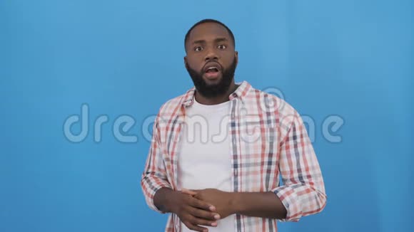 英俊的非裔美国男人穿着蓝色backgrayund的休闲t恤在手臂上获得成功时感到惊讶和惊讶视频的预览图